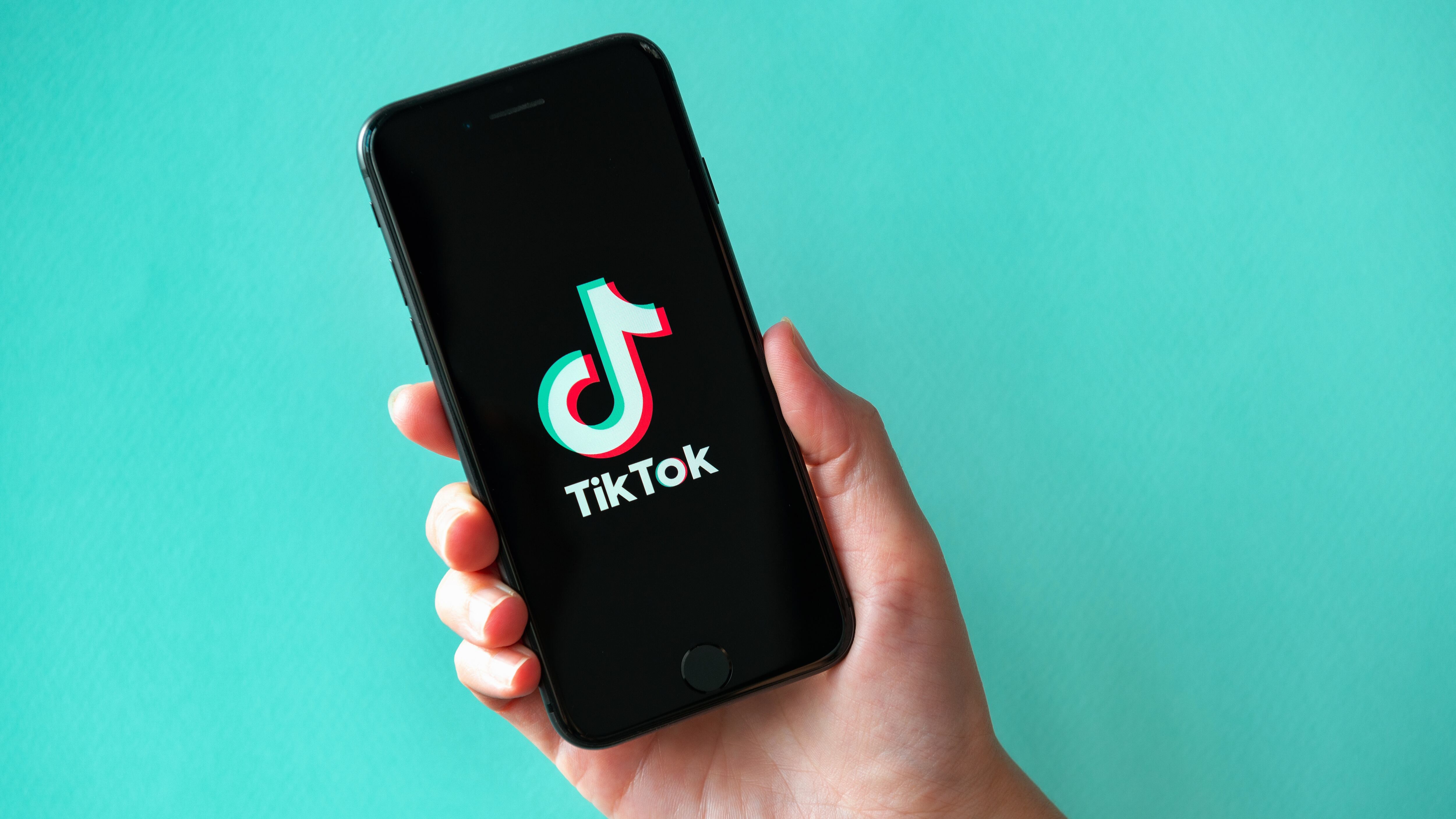 Studio shot of hand holding Apple iPhone 8 with TikTok logotype on a screen.