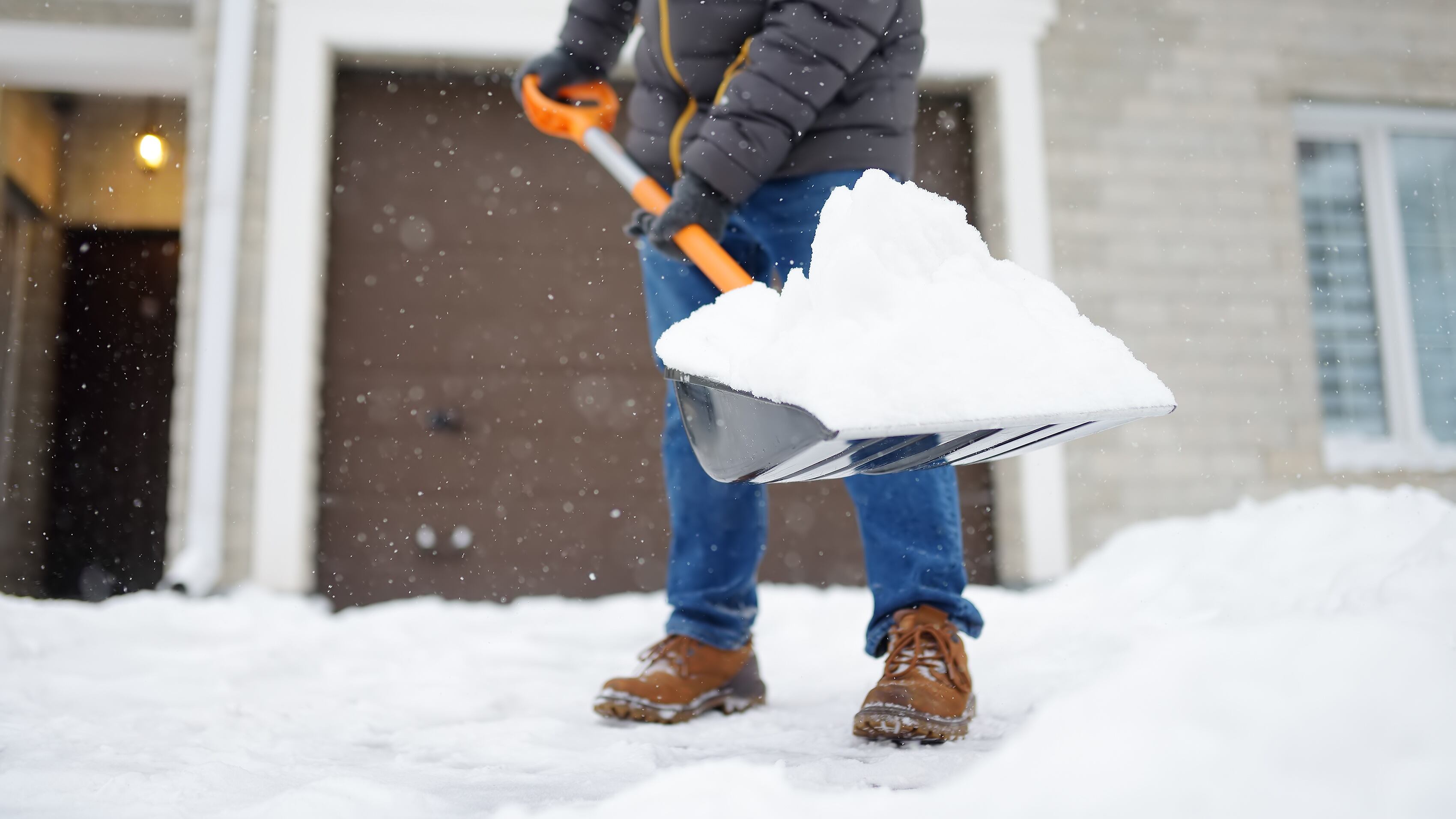 A mature man clean path near house from snow during strong blizzard. Person shoveling snow out of the driveway. Huge snowdrifts. Difficult situation in the city after a snow storm